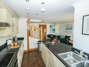 A modern kitchen with a central island, built-in appliances, and a dining area with a green sofa and a coffee table. - 2 Court Cottage, Hillfield Village (Dartmouth)