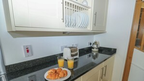 Een keuken met een zwart aanrecht, een bord croissants, twee glaasjes sinaasappelsap, een broodrooster en een waterkoker.