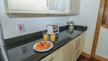 Uma cozinha com bancada preta, um prato de croissants, dois copos de suco de laranja, uma torradeira e uma chaleira.