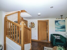Una escalera con barandas de madera, un sillón verde, un cuadro en la pared y una puerta que da a otra habitación.