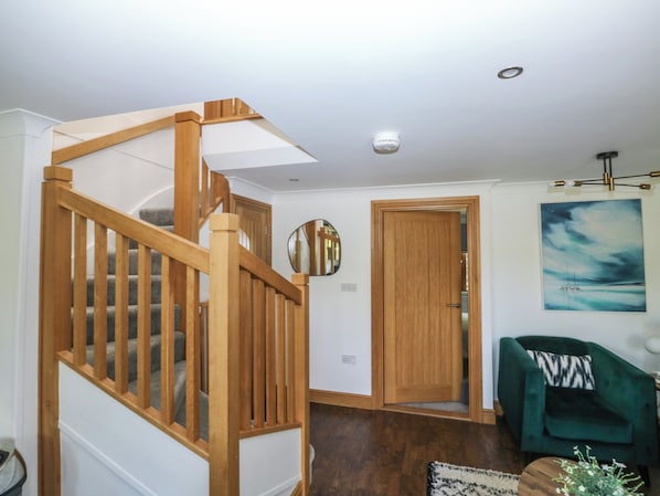 A staircase with wooden railings, a green armchair, a painting on the wall, and a door leading to another room. - 2 Court Cottage, Hillfield Village (Dartmouth)