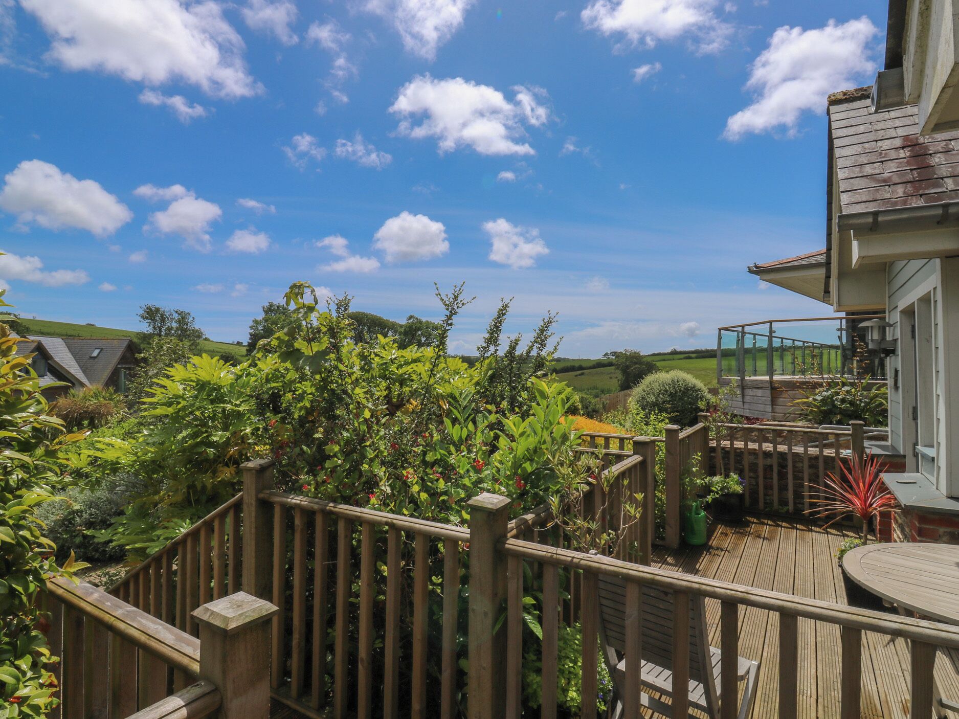 A wooden deck with a railing, surrounded by lush greenery and a clear blue sky.