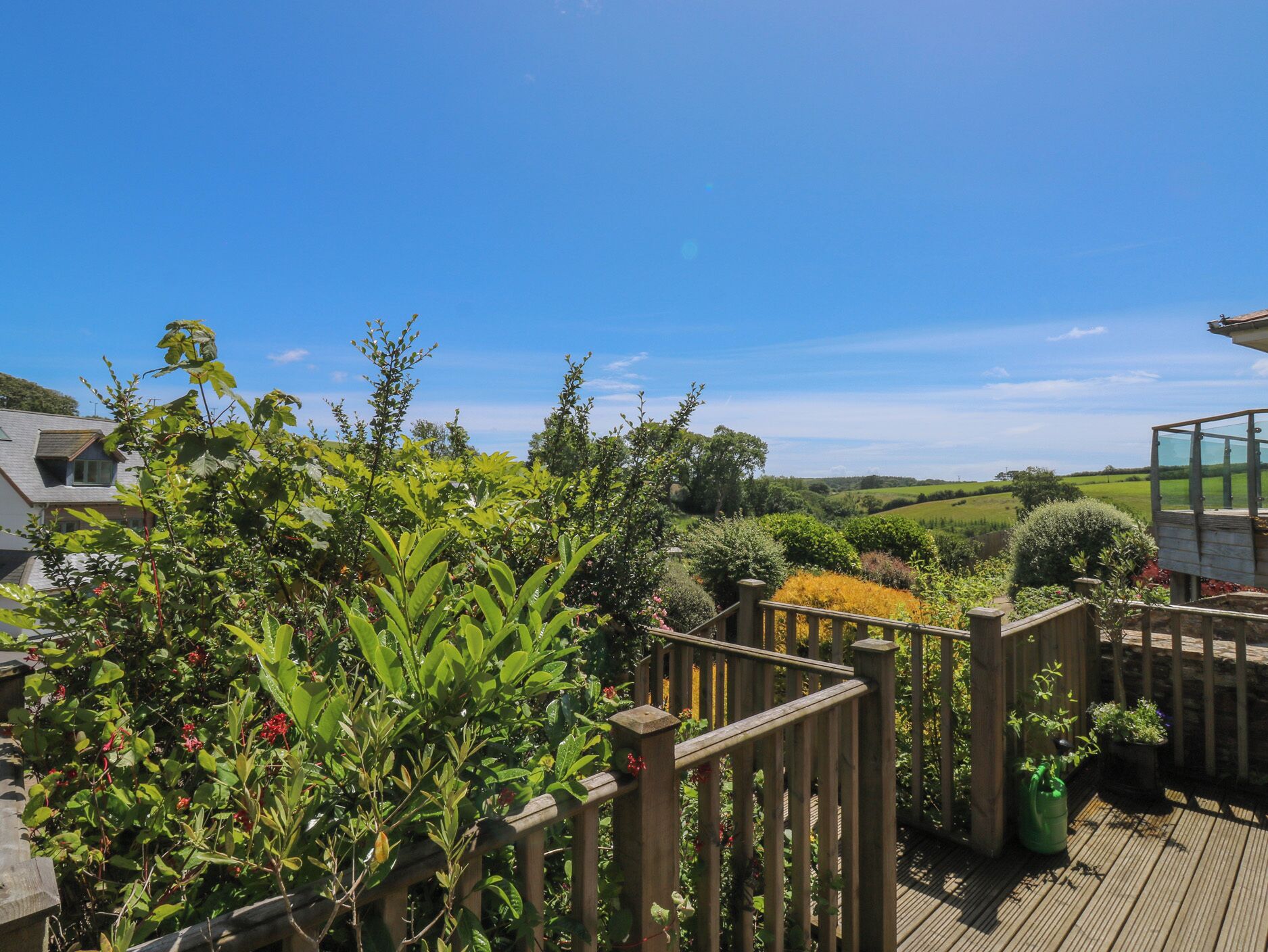 Terraza de madera con vistas a un paisaje rural, cerramiento de vidrio y diversas plantas.