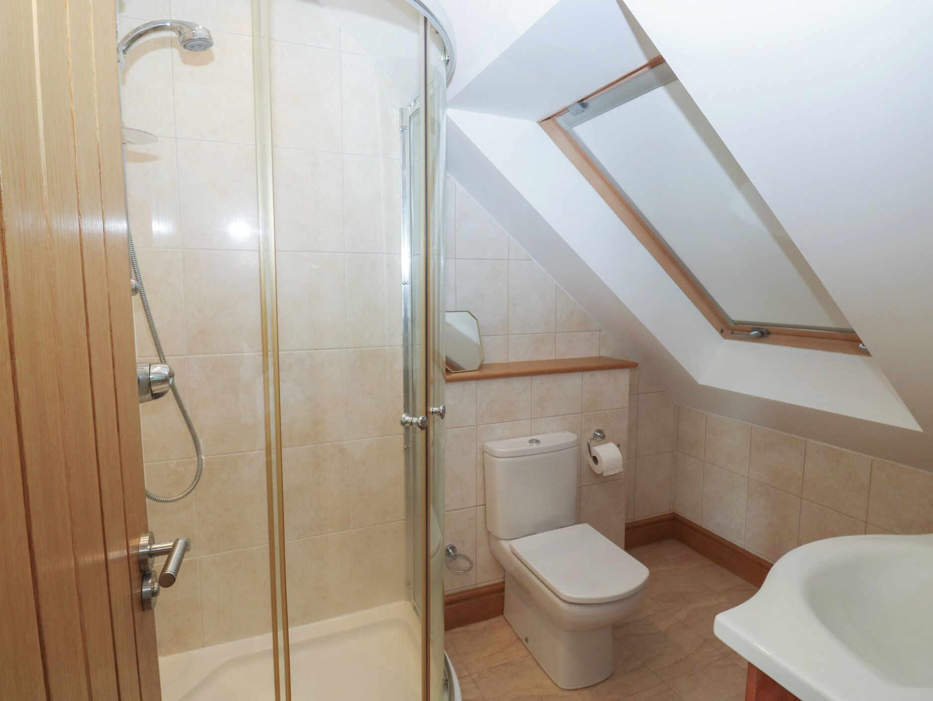 A bathroom with a shower, toilet, and bathtub, featuring a sloped ceiling and wooden door.