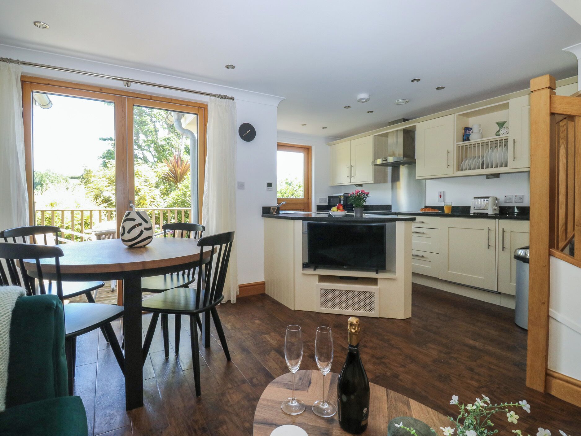 Una cocina con comedor, televisor y una botella de champán.