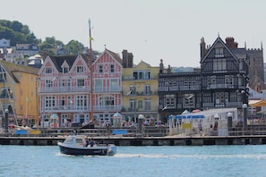 Eine Stadt am Wasser mit bunten Häusern, einem Anleger mit einem Boot und einer Pier mit Menschen.