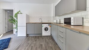 Une cuisine moderne avec des meubles gris, un lave-linge, un four à micro-ondes et une plante en pot.