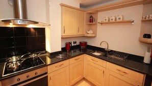 A modern kitchen with a gas stove, wooden cabinets, and a black countertop. - The View in Newcastle Upon Tyne (Newcastle Upon Tyne)