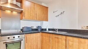 Een moderne keuken met houten kastjes, roestvrijstalen apparatuur en een zwart aanrecht.