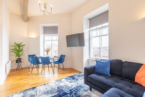 Ein modernes Wohnzimmer mit Sofa, einem Esstisch mit Stühlen, einem an der Wand befestigten Fernseher und großen Fenstern.