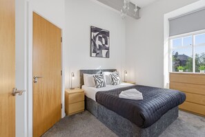 Ein Schlafzimmer mit Bett, Nachttischen, einem Fenster und einer Tür.