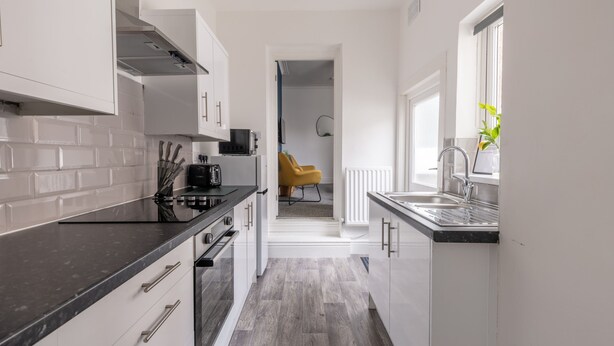 Una cocina moderna con armarios blancos, encimera negra y una ventana con una planta.
