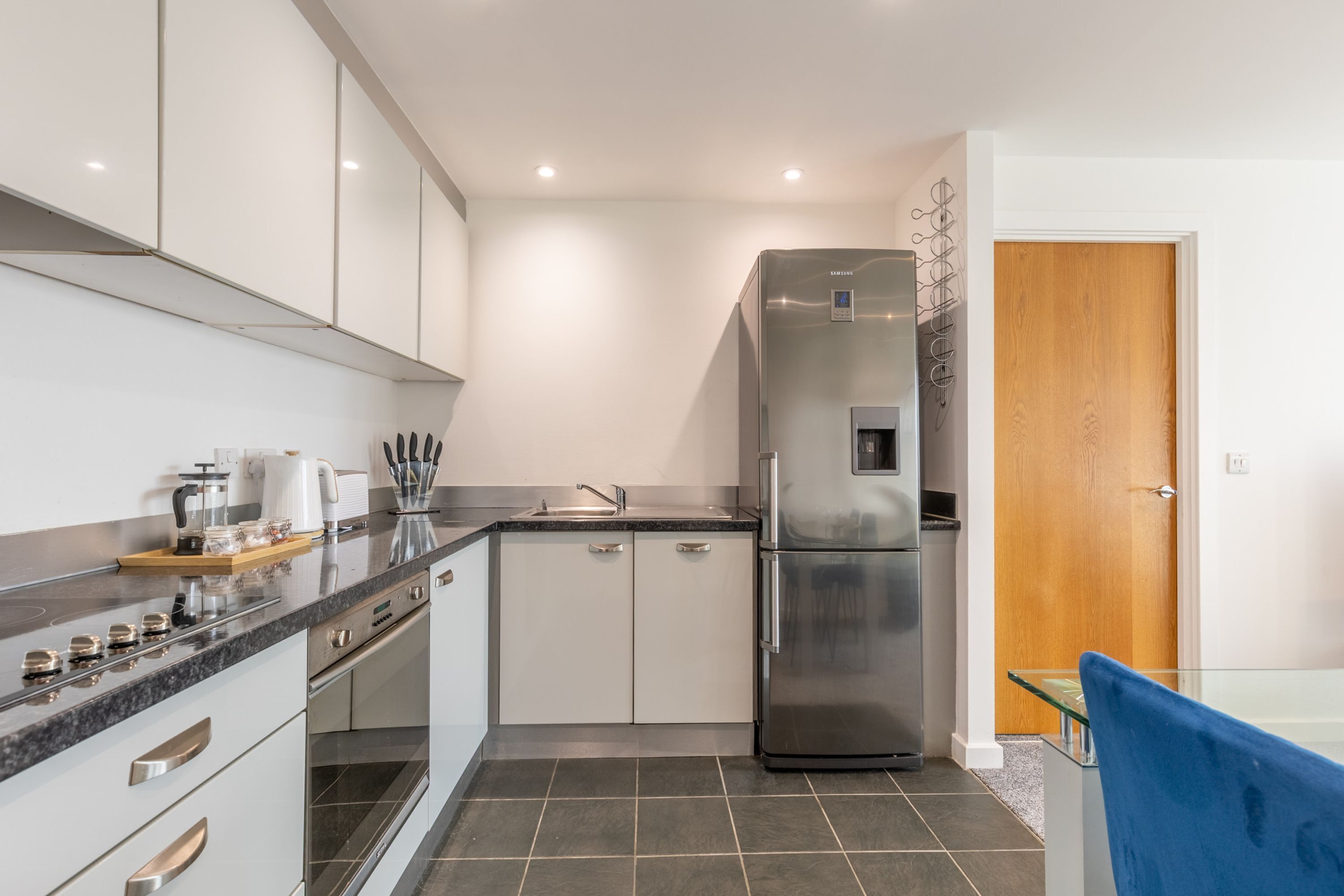 A modern kitchen with white cabinets, a stainless steel refrigerator, and a built-in oven.