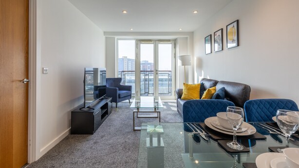 A modern living room with a glass coffee table, a sofa with blue cushions, and a dining area set with plates and glasses. - Waterloo in Newcastle Upon Tyne (Newcastle Upon Tyne)