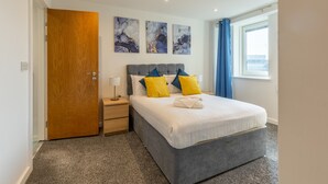 A modern hotel room with a grey bed, blue and yellow pillows, a wooden door, and marble artwork on the wall. - Waterloo in Newcastle Upon Tyne (Newcastle Upon Tyne)