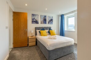 Ein modernes Hotelzimmer mit einem grauen Bett, blau-gelben Kissen, einer Holztür und Marmorbildkunst an der Wand.