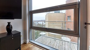 Ein Zimmer mit großem Fenster, einem Flachbildfernseher, einem schwarzen Schrank und einem weißen Stuhl.