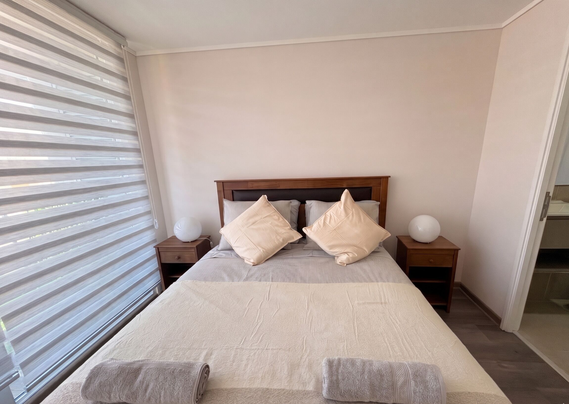 Une chambre à coucher avec un lit, deux tables de chevet et une fenêtre avec des stores.
