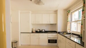 Una cocina con armarios blancos, encimera negra, un fregadero y una ventana con cortinas.