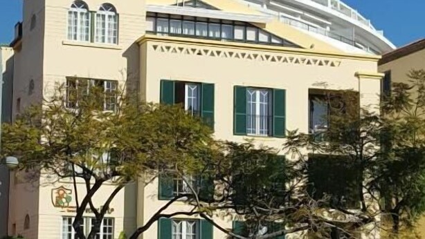 Un edificio de varios pisos con techo plano, contraventanas verdes y un balcón.