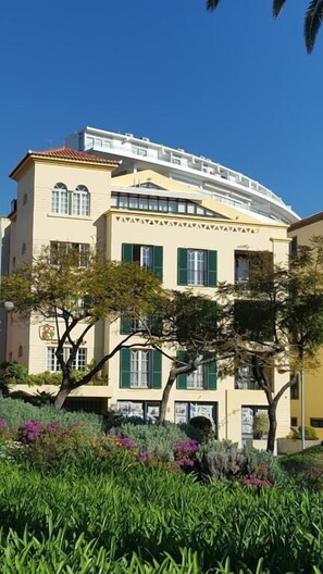 Um edifício de vários andares com telhado plano, persianas verdes e uma varanda.