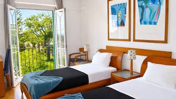 Quarto de hotel com duas camas, varanda com vista para vegetação e duas obras de arte emolduradas na parede.