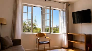 Quarto com sofá, cadeira, mesa, televisão e janela com cortinas.