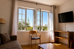 Quarto com sofá, cadeira, mesa, televisão e janela com cortinas.