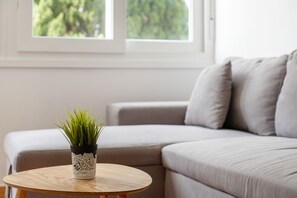 A room with a round wooden table, a potted plant, and a grey sofa.