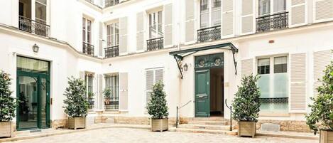 A courtyard with a central entrance, potted plants, and a building with multiple windows and balconies.