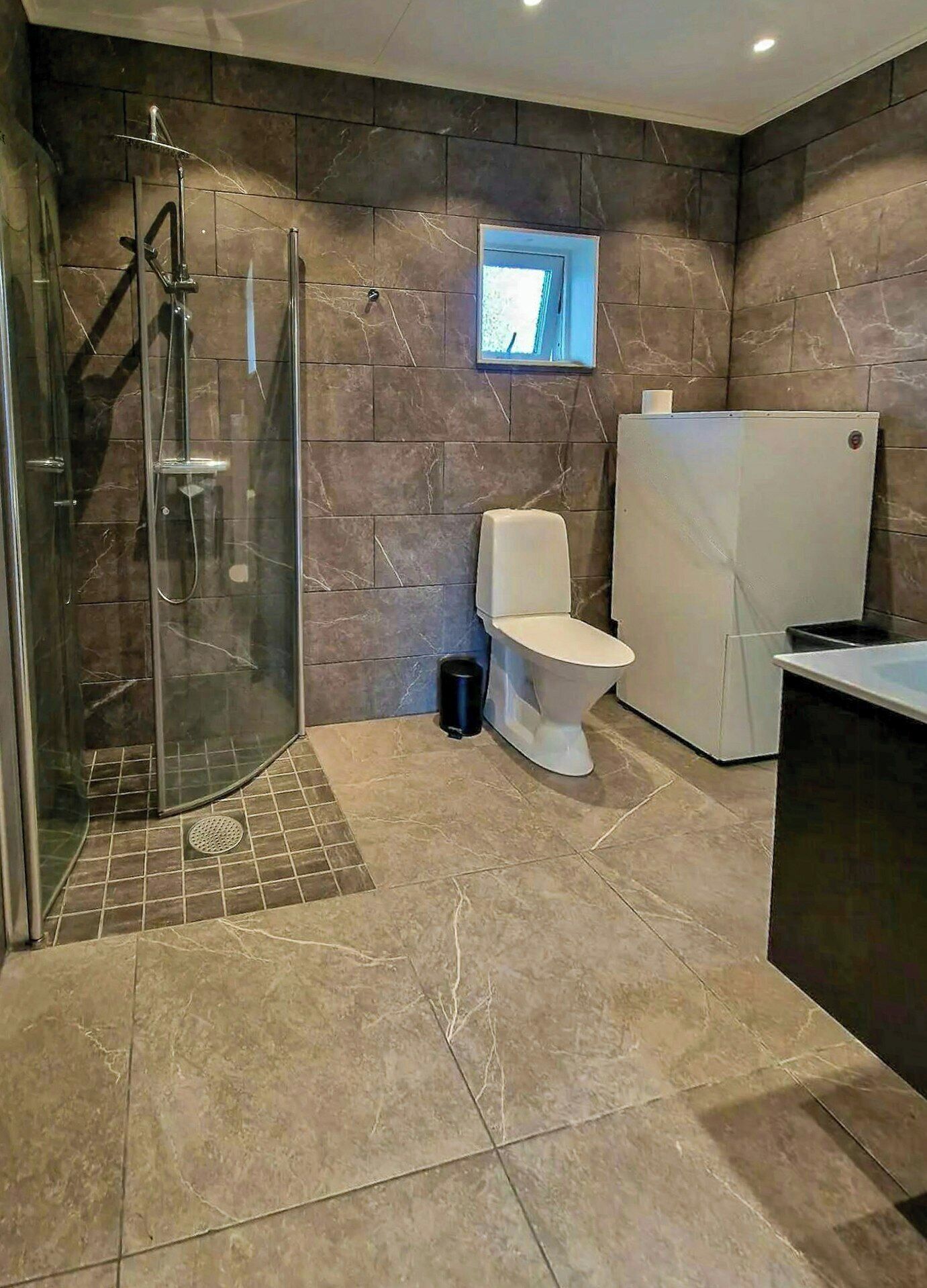 Un baño con ducha, inodoro y un ventanal pequeño.