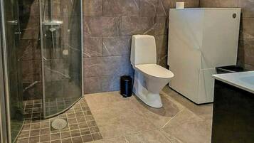 Un baño con ducha, inodoro y un ventanal pequeño.
