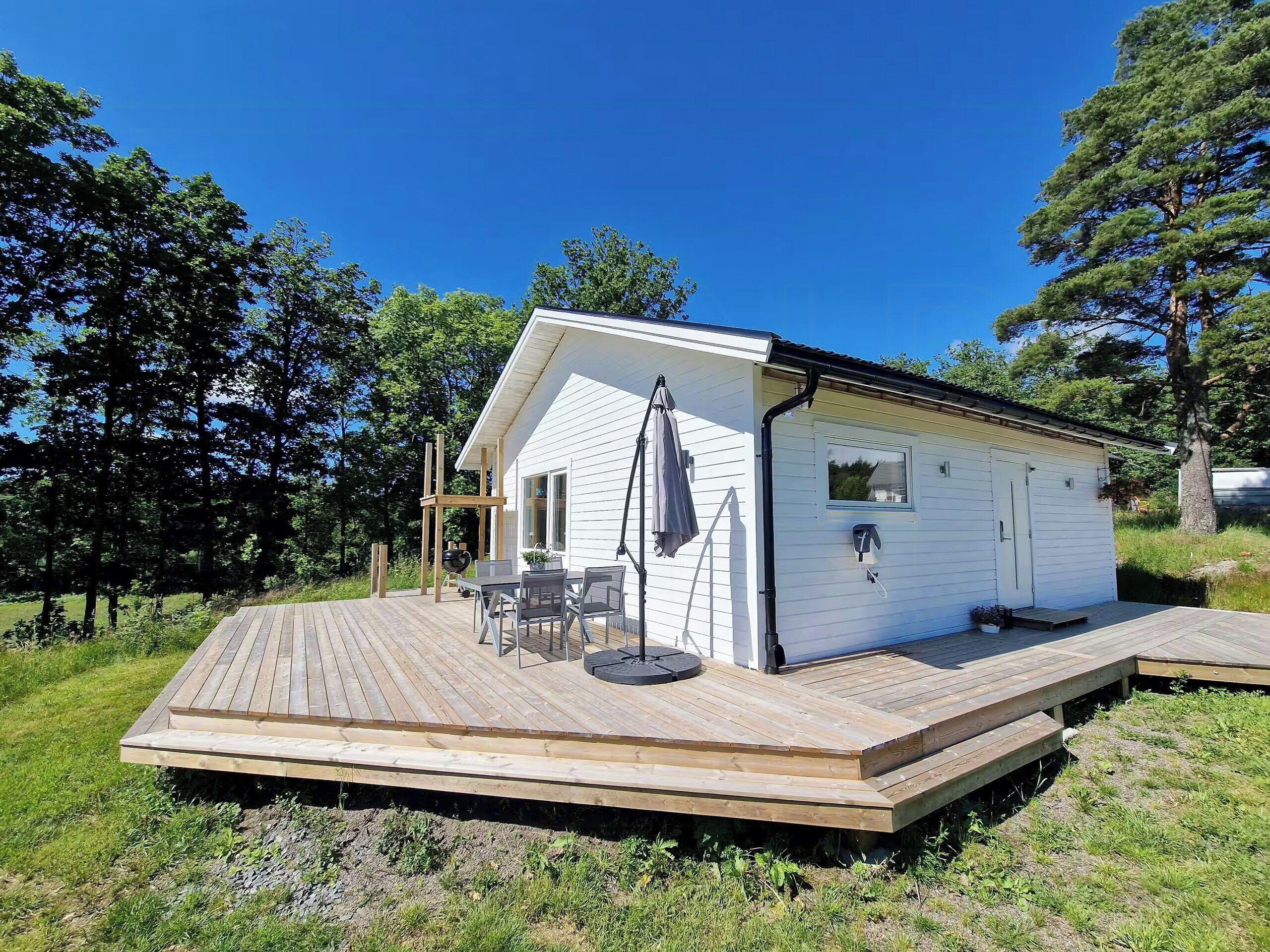 A small, single-story cabin with a deck, a table and chairs, and a covered outdoor seating area.