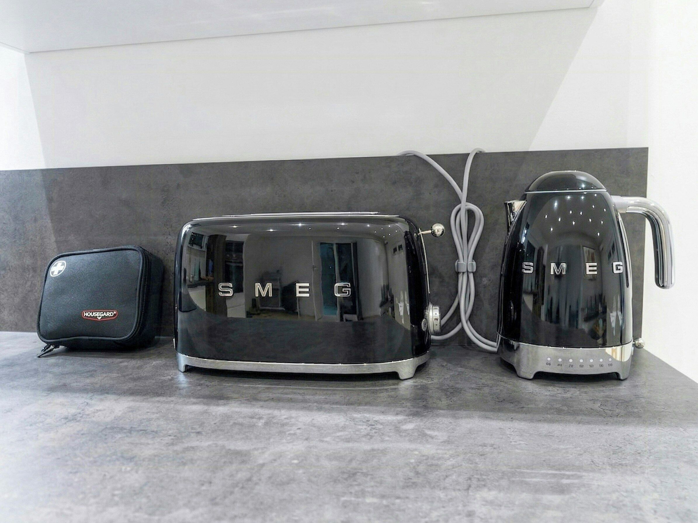 Una cocina con un tostador negro, un hervidor y un aparato Housegard negro sobre una encimera gris.