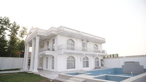 Una casa grande y blanca de dos pisos con piscina, balcón y césped bien cuidado.