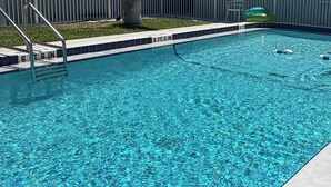 Une piscine avec un palmier, une clôture blanche et un bâtiment doté de balcons en arrière-plan.