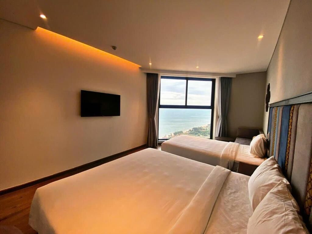A hotel room with two beds, a large window with a view, and a flat-screen TV mounted on the wall.