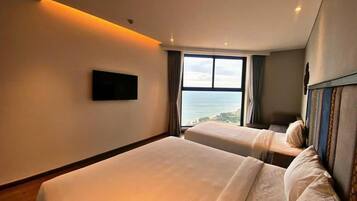 A hotel room with two beds, a large window with a view, and a flat-screen TV mounted on the wall.