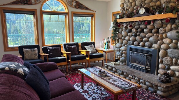 A cozy living room with a fireplace, stone wall, and large windows.