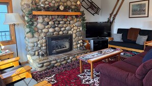 A cozy living room with a stone fireplace, a television, a sofa, and a coffee table.