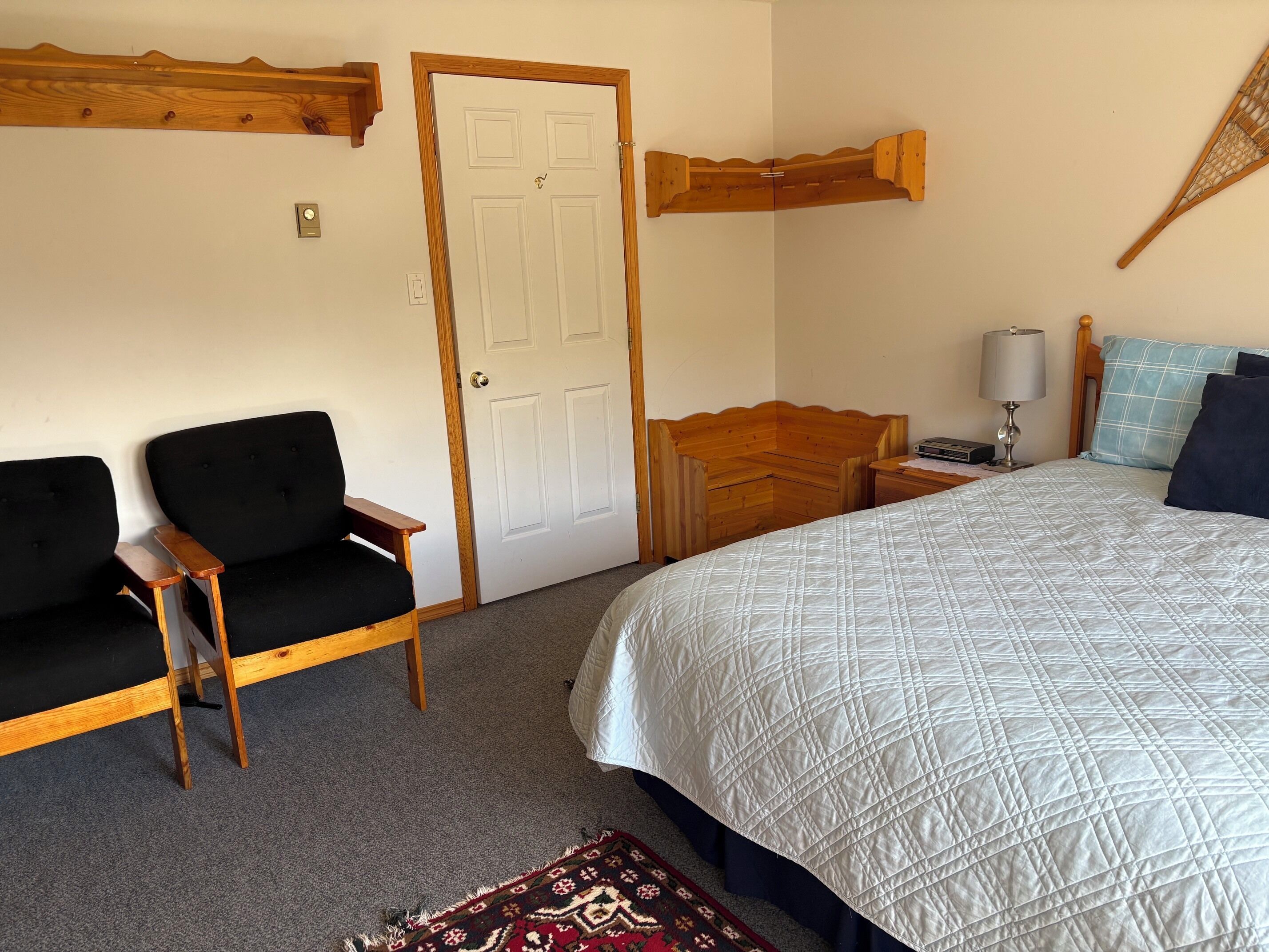 Une chambre à coucher avec un lit, une chaise, une table de chevet en bois, une lampe et une porte.