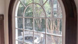 A large arched window with multiple panes, offering a view of an outdoor seating area with a curved sofa and a fire pit.