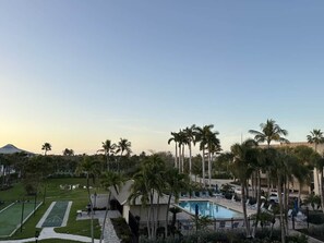 A resort with a swimming pool, palm trees, and a tennis court. - Sanibel Sunrise 3 bed 3 bath Beachfront Condo (Sanibel)