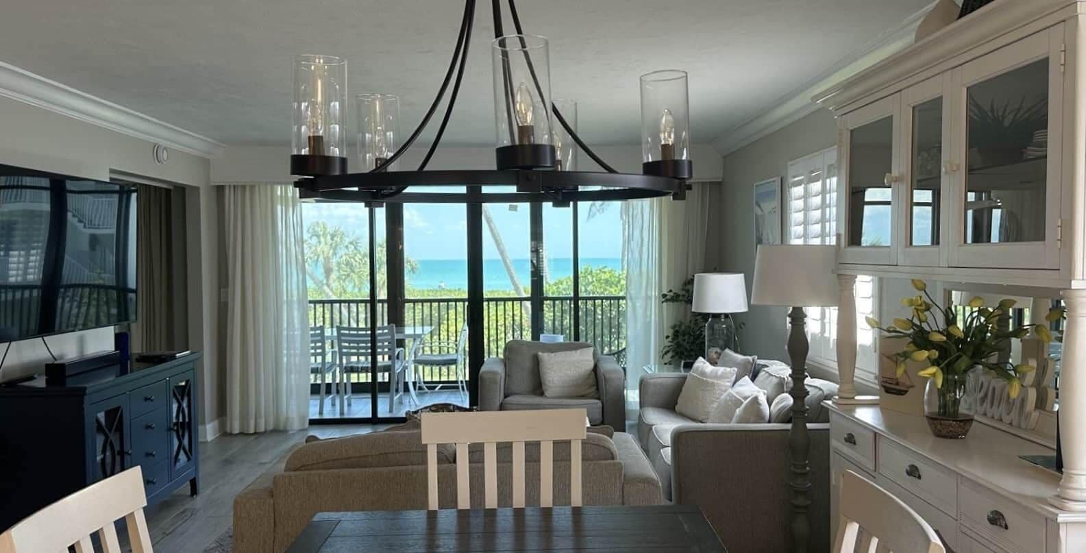 A living room with a TV, dining table, sofa, and a view of the ocean.