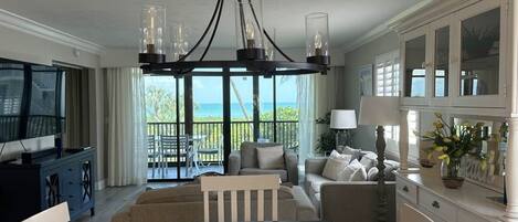 A living room with a TV, dining table, sofa, and a view of the ocean.