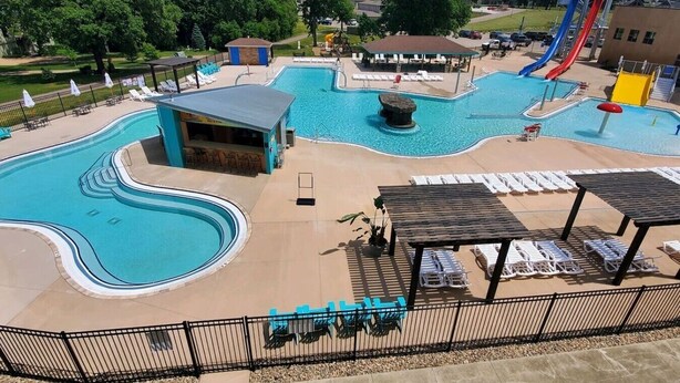 Una piscina con uno scivolo, lettini e una zona relax coperta.