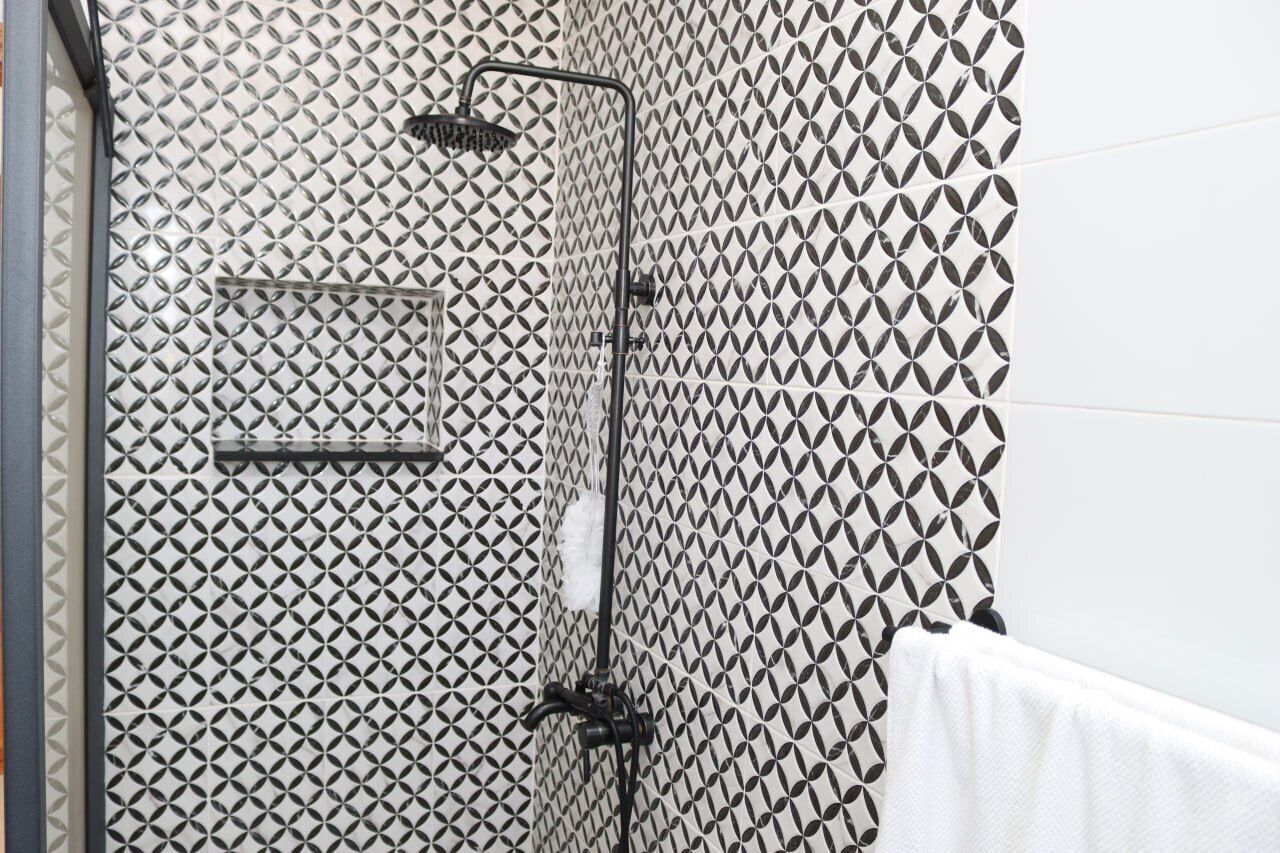 A bathroom with a geometric patterned wall, a shower with a handheld showerhead, and a towel rack.