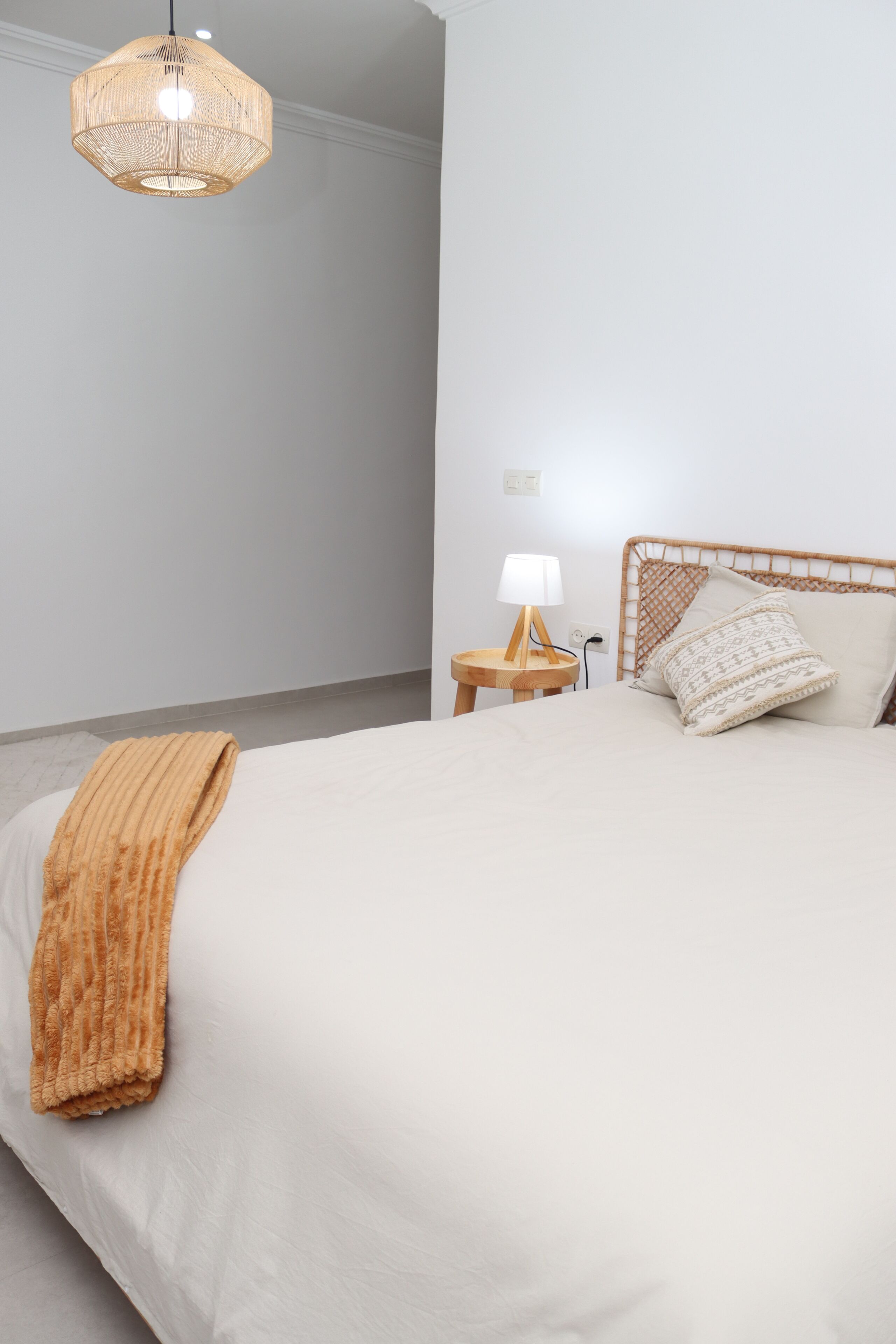 A bedroom with a large bed, a bedside table with a lamp, and a hanging light fixture.