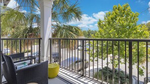 A balcony with wicker furniture, a yellow cushion, and a view of a parking lot and trees.