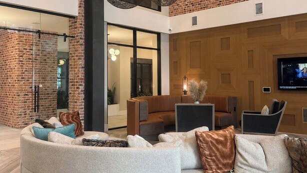 A modern interior with a curved sectional sofa, a round coffee table with a plant, and a brick wall.